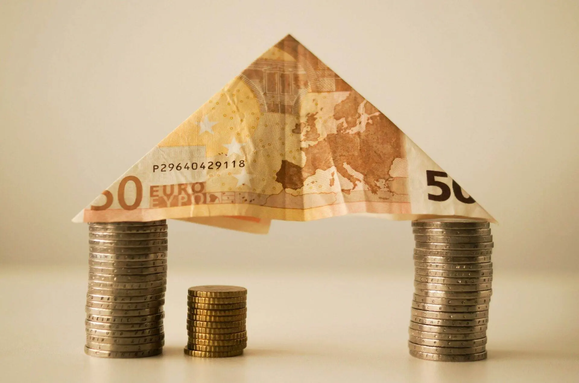 Symbolische Darstellung der Immobilienbewertung in Wien: Ein Dach aus einem 50-Euro-Schein ruht auf Stapeln von Münzen, die verschiedene Wertstufen darstellen. Diese bildliche Darstellung verdeutlicht den finanziellen Aspekt und die Bedeutung der monetären Bewertung von Immobilien in Wien.