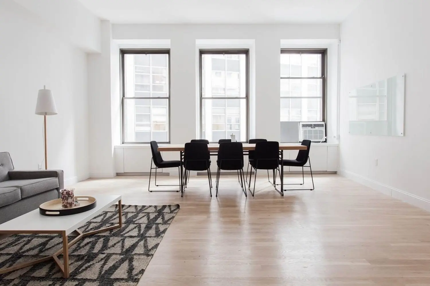 Zur Vermietung steht ein minimalistischer Wohn- und Essbereich mit hellem Holzboden zur Verfügung. Er verfügt über ein graues Sofa, einen geometrischen Teppich, einen modernen Couchtisch und einen Esstisch mit schwarzen Stühlen. Drei große Fenster lassen Tageslicht herein und verleihen dem Raum Helligkeit. Zur Vermietung steht ein minimalistischer Wohn- und Essbereich mit hellem Holzboden zur Verfügung. Er verfügt über ein graues Sofa, einen geometrischen Teppich, einen modernen Couchtisch und einen Esstisch mit schwarzen Stühlen. Drei große Fenster lassen Tageslicht herein und verleihen dem Raum Helligkeit.
