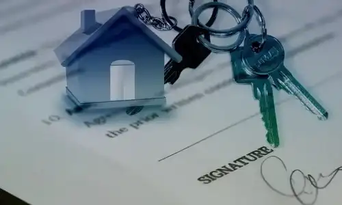Nahaufnahme eines Dokuments mit einer Unterschrift darunter und einem Schlüsselbund, der an einem hausförmigen Schlüsselanhänger befestigt ist. Der Fokus auf die Schlüssel deutet auf Eigentums- oder Immobilienthemen hin – ideal für diejenigen, die mit Vires Immobilienmakler in Wien eine Wohnung verkaufen möchten.